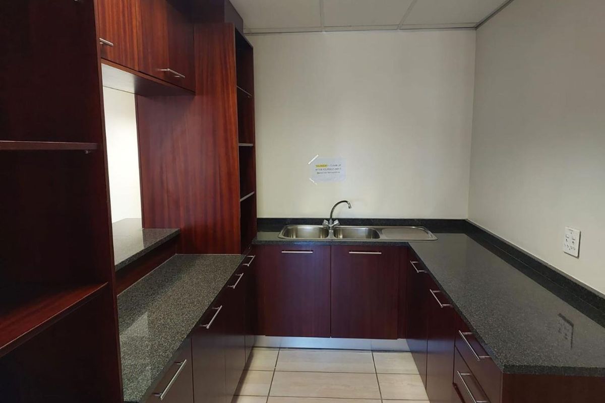 A functional office kitchenette featuring dark wood cabinetry, granite countertops, and a double stainless steel sink.