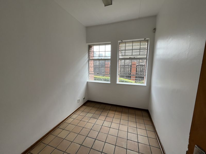 A compact, empty office space featuring tiled flooring and dual windows with security bars, offering a functional area for a workspace.