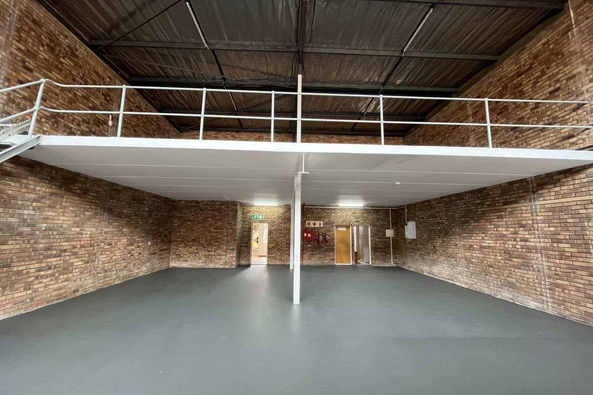 Spacious industrial warehouse unit featuring exposed brick walls, a mezzanine level with safety railing, and a clean epoxy-coated floor.