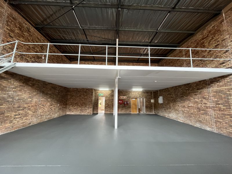 Spacious industrial warehouse unit featuring exposed brick walls, a mezzanine level with safety railing, and a clean epoxy-coated floor.