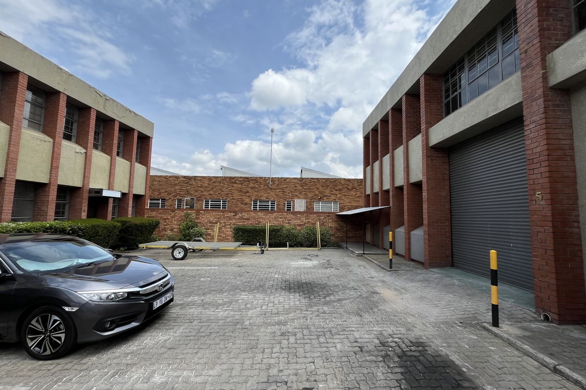 Exterior view of an industrial property featuring a paved courtyard, brick facade, and a large roller shutter door for vehicle access.