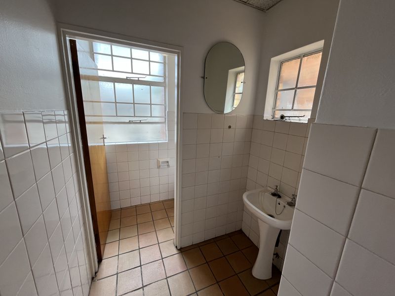 A functional industrial-style bathroom featuring a pedestal basin, tiled walls and flooring, and natural light from steel-framed windows.