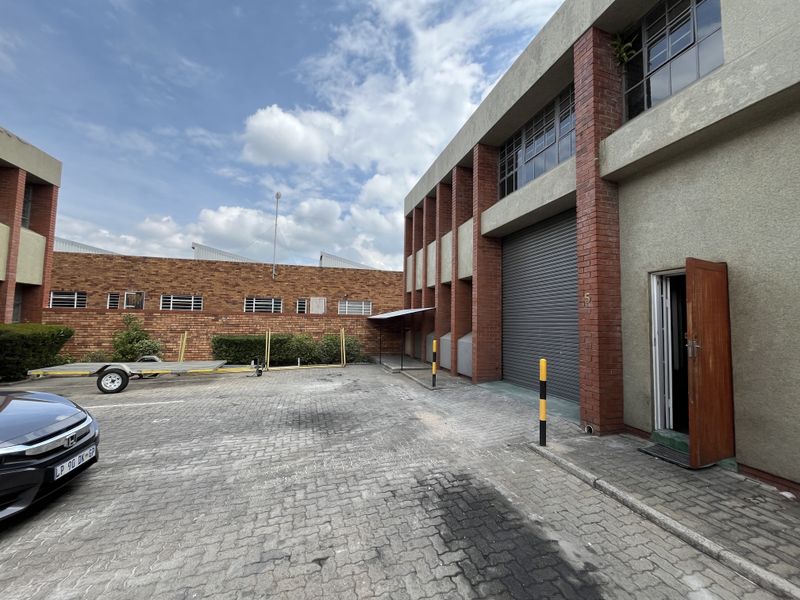 Industrial property exterior featuring a roller shutter door, brick facade, and paved driveway access.