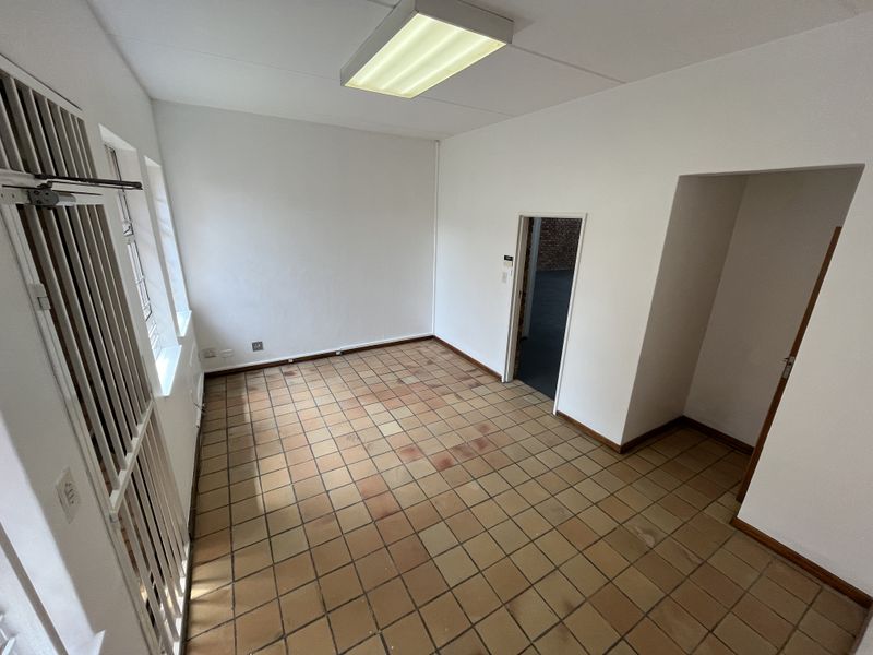 An empty office space featuring ceramic tile flooring, fluorescent lighting, and security bars on the windows, suitable for a professional workspace.