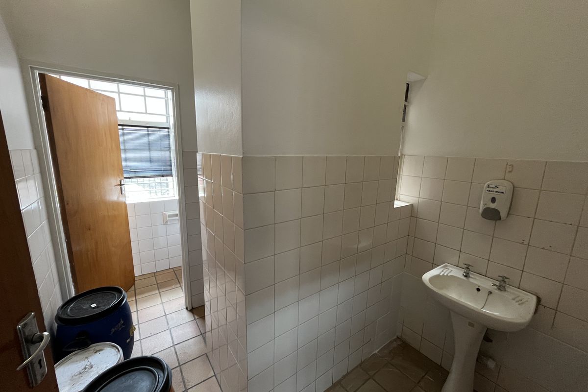 A functional industrial bathroom featuring a pedestal basin, tiled walls, and tiled flooring, providing basic utility and sanitation facilities.