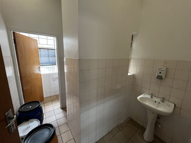 A functional industrial bathroom featuring a pedestal basin, tiled walls, and tiled flooring, providing basic utility and sanitation facilities.
