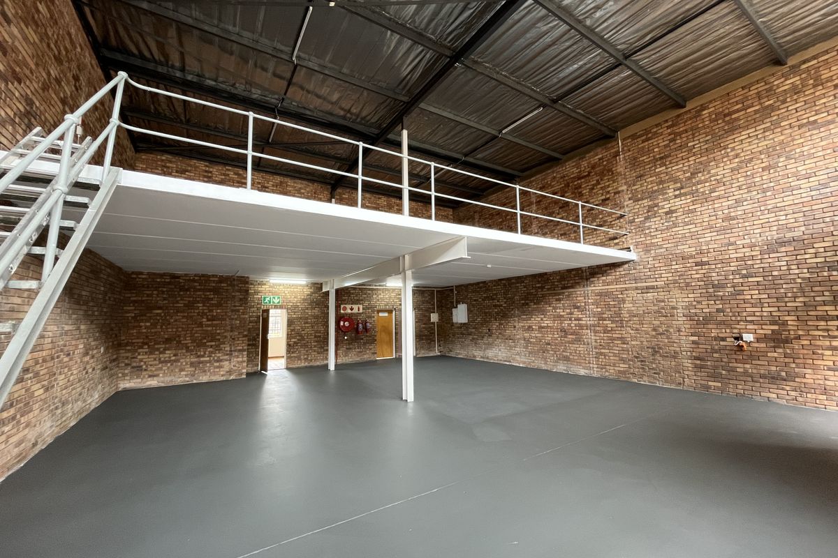 Spacious industrial warehouse unit featuring a mezzanine level, exposed brickwork, high ceilings with exposed steel structure, and a clean painted concrete floor.