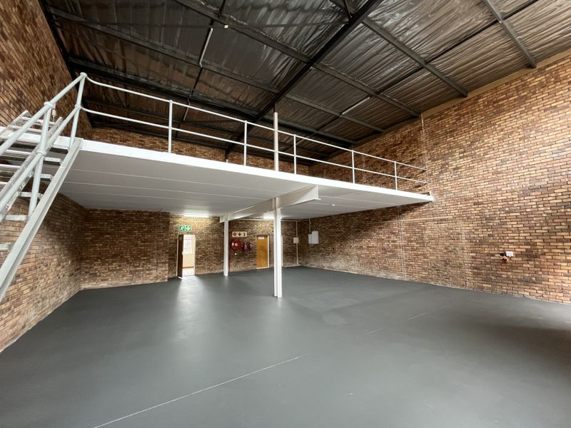 Spacious industrial warehouse unit featuring a mezzanine level, exposed brickwork, high ceilings with exposed steel structure, and a clean painted concrete floor.