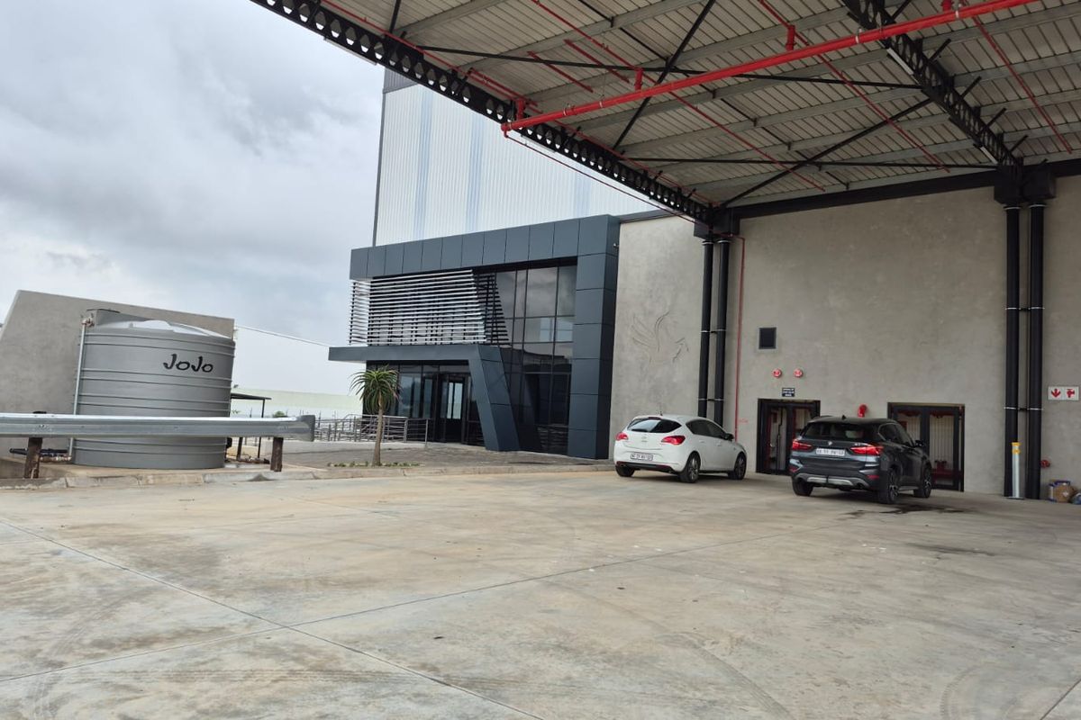 Industrial facility exterior featuring a large covered loading area, concrete hardstand, and modern glass-fronted office entrance with a water storage tank.