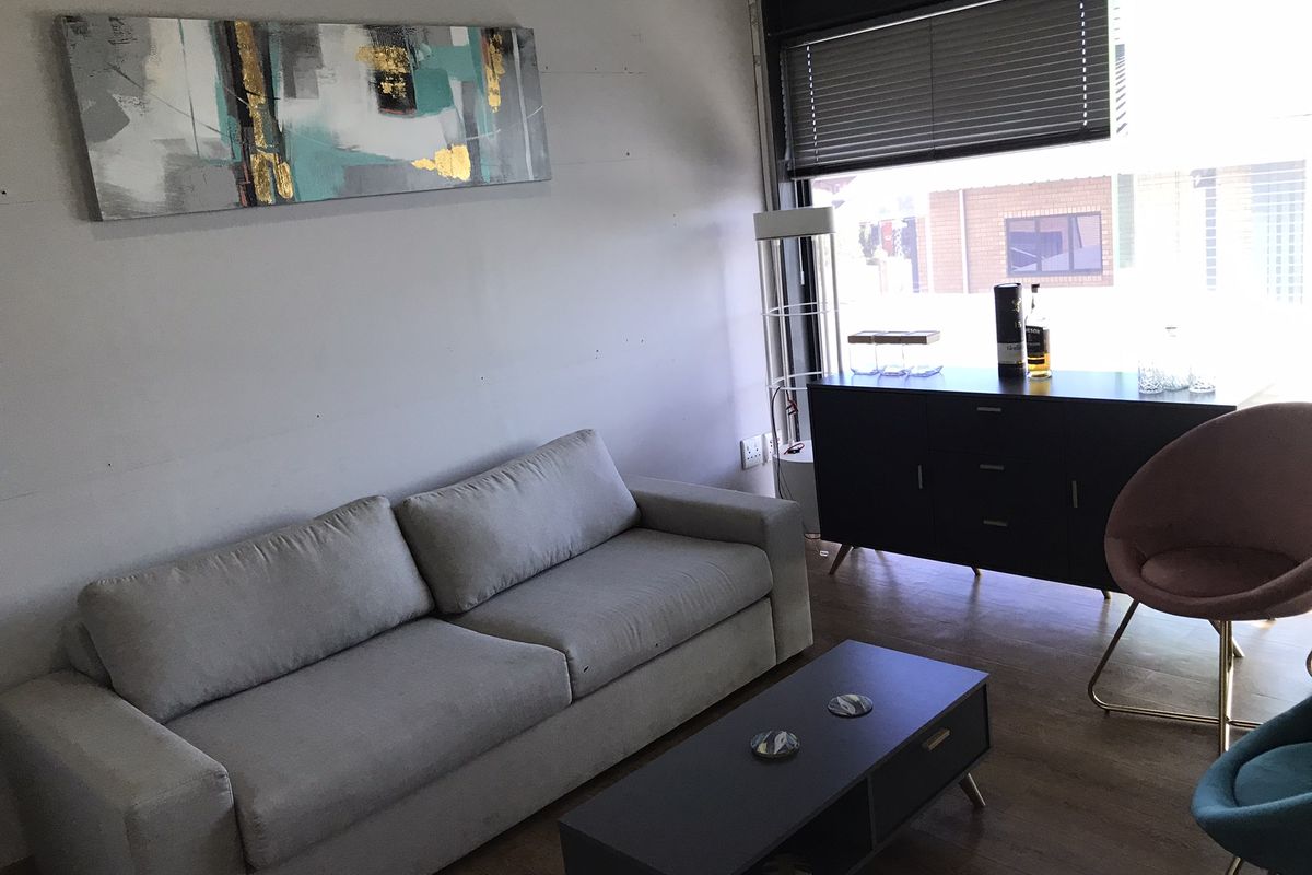 A functional living area featuring wood-look flooring, large window with fitted blinds, and neutral wall finishes.