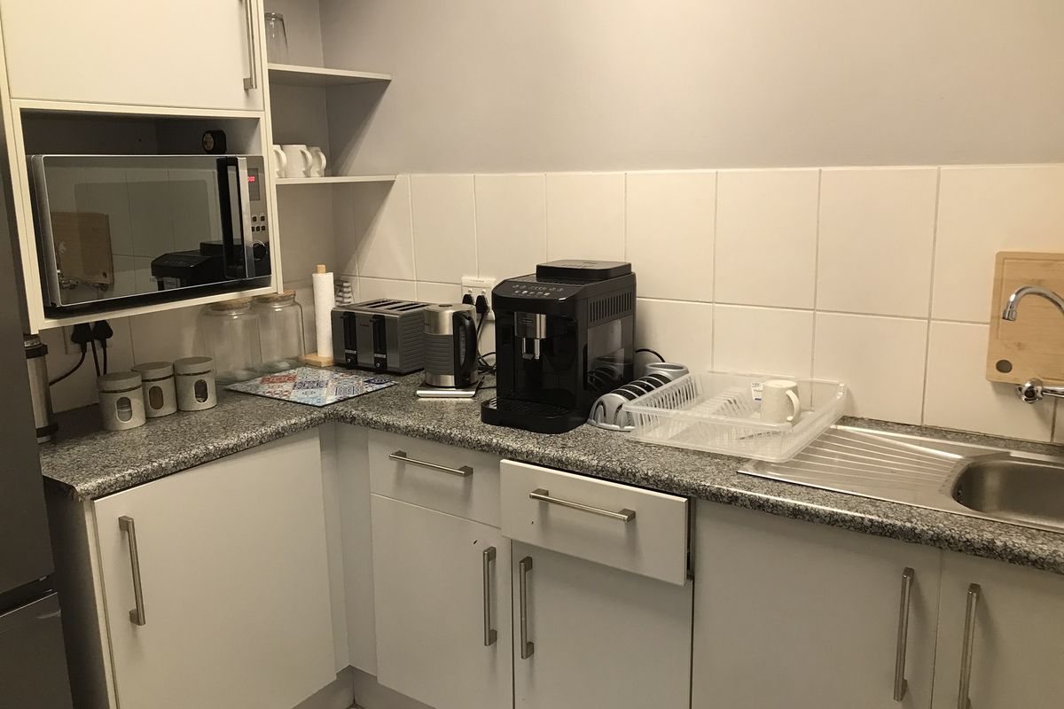 Compact kitchen area featuring white cabinetry, granite-style countertops, a stainless steel sink, and built-in microwave housing.