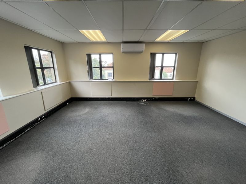 A vacant office space featuring a suspended ceiling, recessed lighting, wall-mounted air conditioning, and perimeter trunking for electrical and data connectivity.
