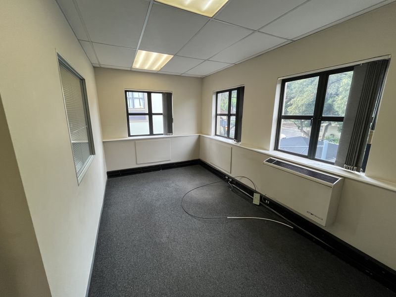 A vacant office space featuring carpeted flooring, a suspended ceiling with recessed lighting, and an integrated HVAC unit with large windows.
