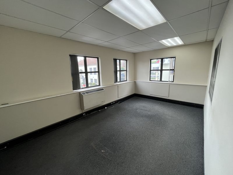 An empty office space featuring a suspended ceiling, recessed lighting, carpeted flooring, and a built-in HVAC unit.
