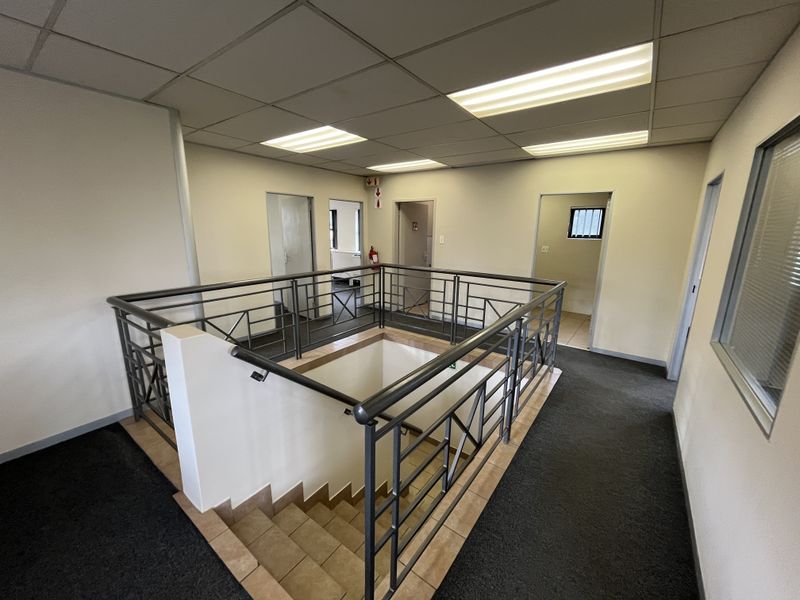 A spacious office building landing featuring a central staircase with metal balustrades, carpeted flooring, and recessed ceiling lighting leading to multiple office doorways.