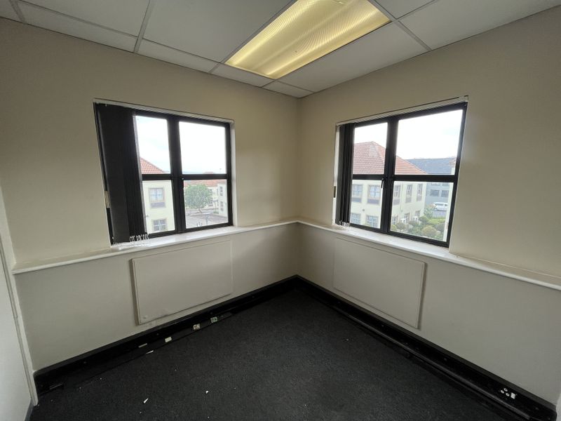 Empty corner office space featuring suspended ceilings, black-framed windows, dado rails, and integrated skirting board trunking for electrical connectivity.
