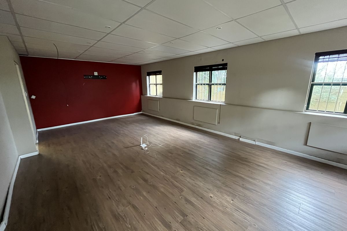 Spacious, empty office area featuring laminate flooring, a suspended ceiling with recessed lighting, and security bars on the windows.