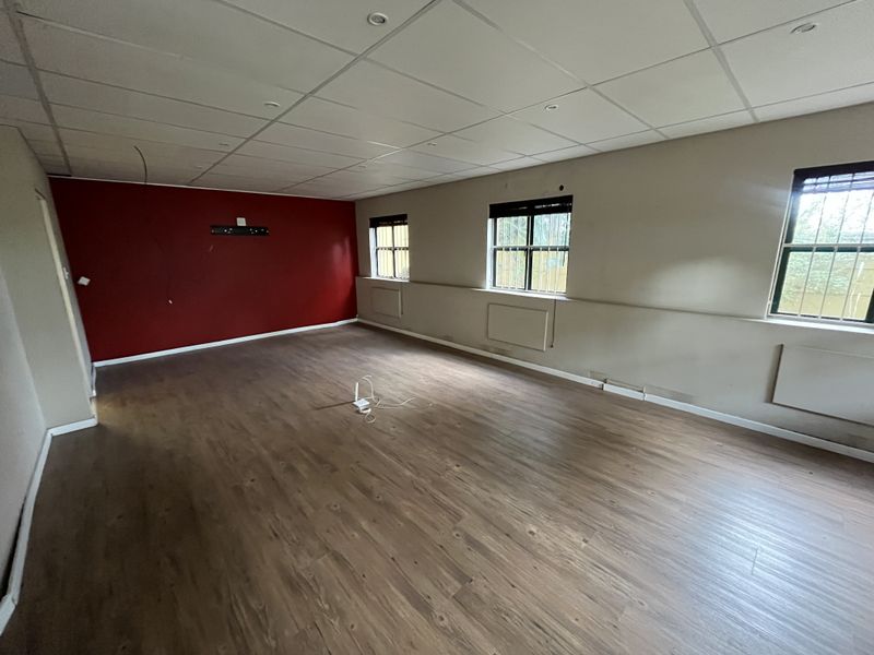 Spacious, empty office area featuring laminate flooring, a suspended ceiling with recessed lighting, and security bars on the windows.