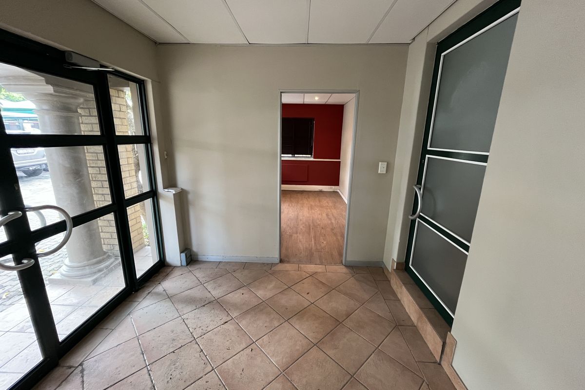 A functional office entrance area featuring tiled flooring, a suspended ceiling, and access to an adjoining office space through a central doorway.