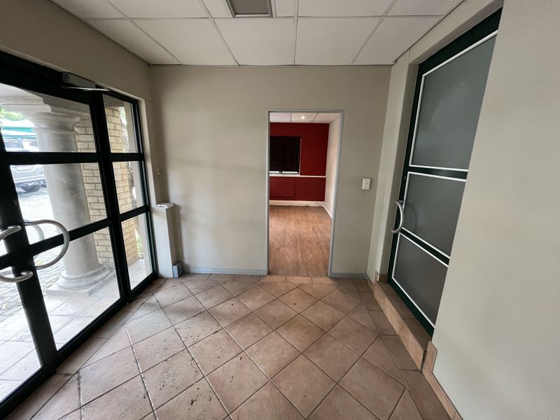 A functional office entrance area featuring tiled flooring, a suspended ceiling, and access to an adjoining office space through a central doorway.