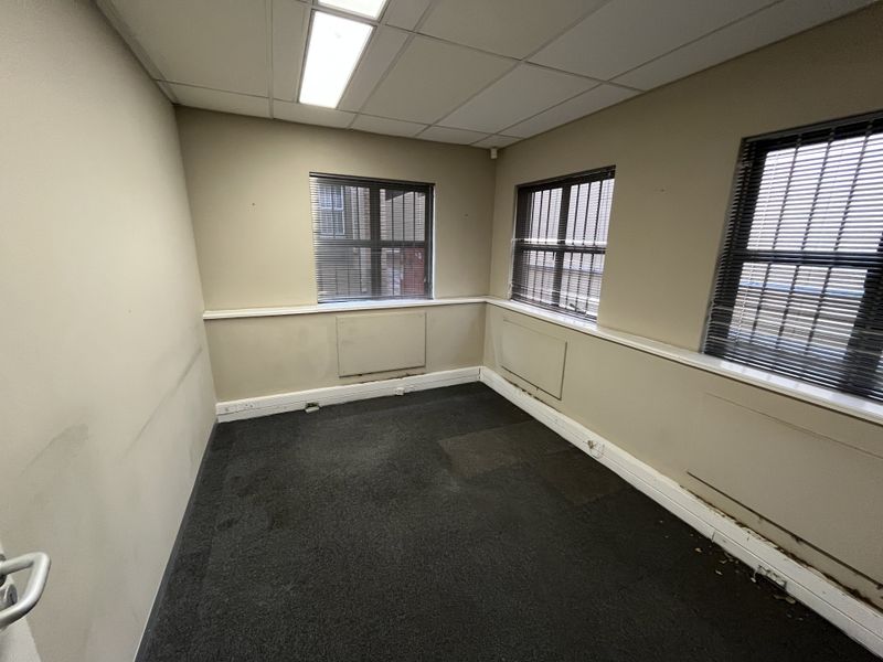 An empty office space featuring carpeted flooring, suspended ceiling with recessed lighting, and multiple windows with fitted blinds.