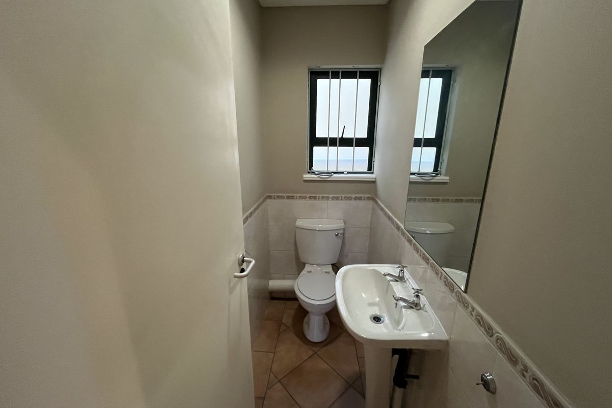 A functional guest bathroom featuring a pedestal basin, toilet, tiled flooring, and a wall-mounted mirror.