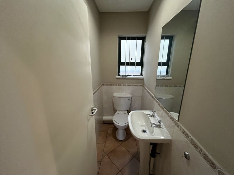 A functional guest bathroom featuring a pedestal basin, toilet, tiled flooring, and a wall-mounted mirror.