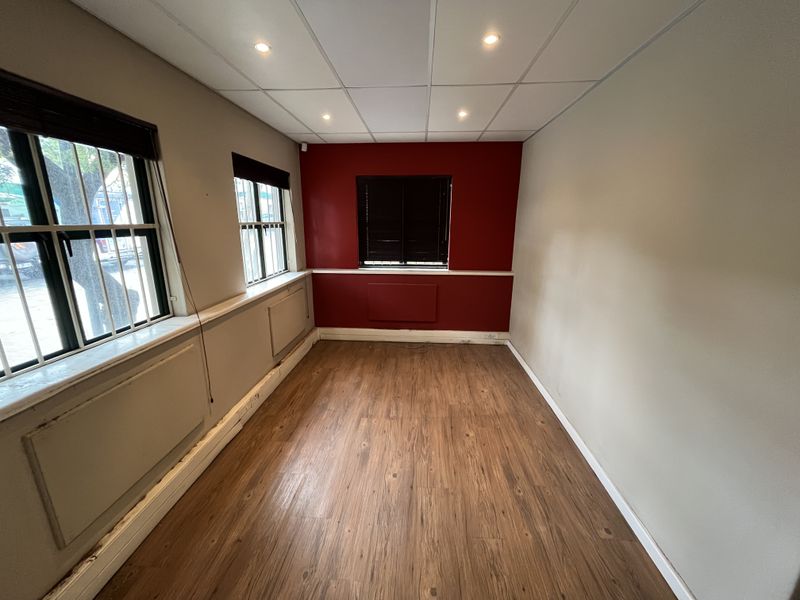 A vacant office space featuring laminate flooring, a suspended ceiling with recessed lighting, and large windows with fitted blinds.