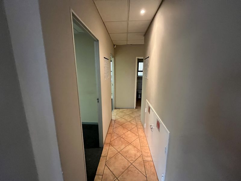 A functional office hallway featuring tiled flooring, a suspended ceiling with recessed lighting, and access to multiple rooms.