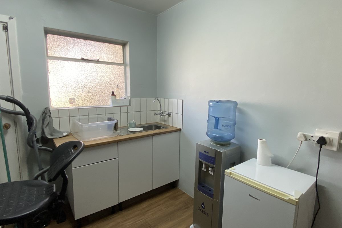 A functional office kitchenette featuring a single sink, wooden countertop, white cabinetry, and tiled splashback.