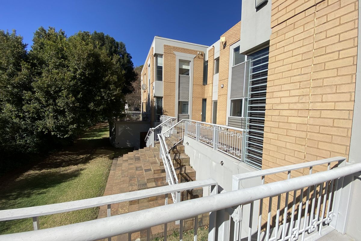 Exterior view of the office building featuring a multi-level brick facade, tiled staircase, and metal safety railings overlooking a landscaped garden area.