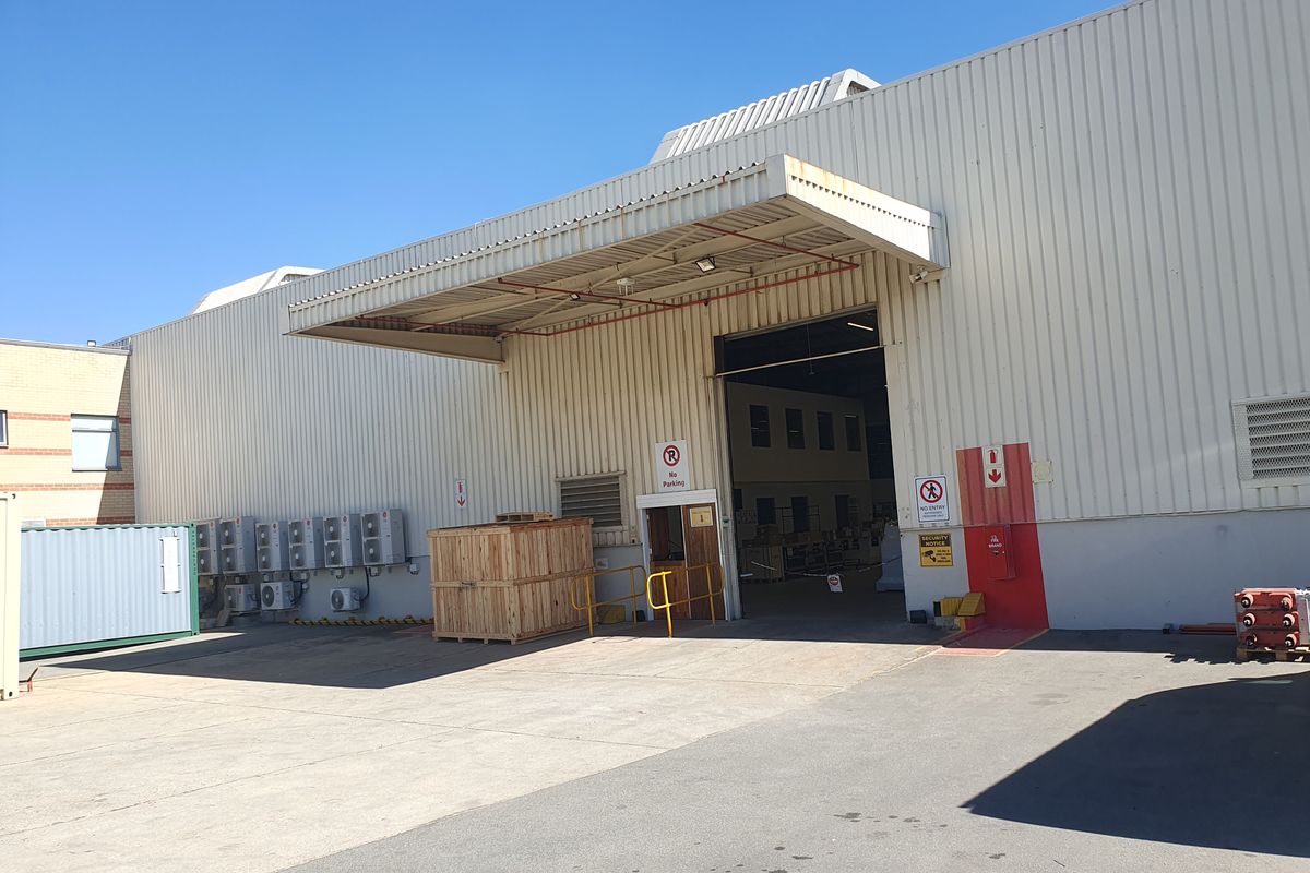 Industrial warehouse exterior featuring a large loading bay with a metal canopy, concrete apron, and multiple wall-mounted HVAC units.