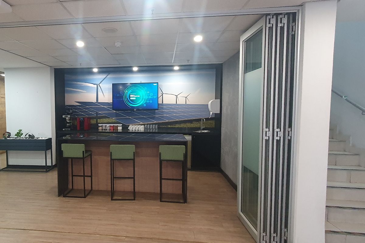 A modern industrial break area featuring a built-in kitchenette, counter seating, and a feature wall with integrated display screen.