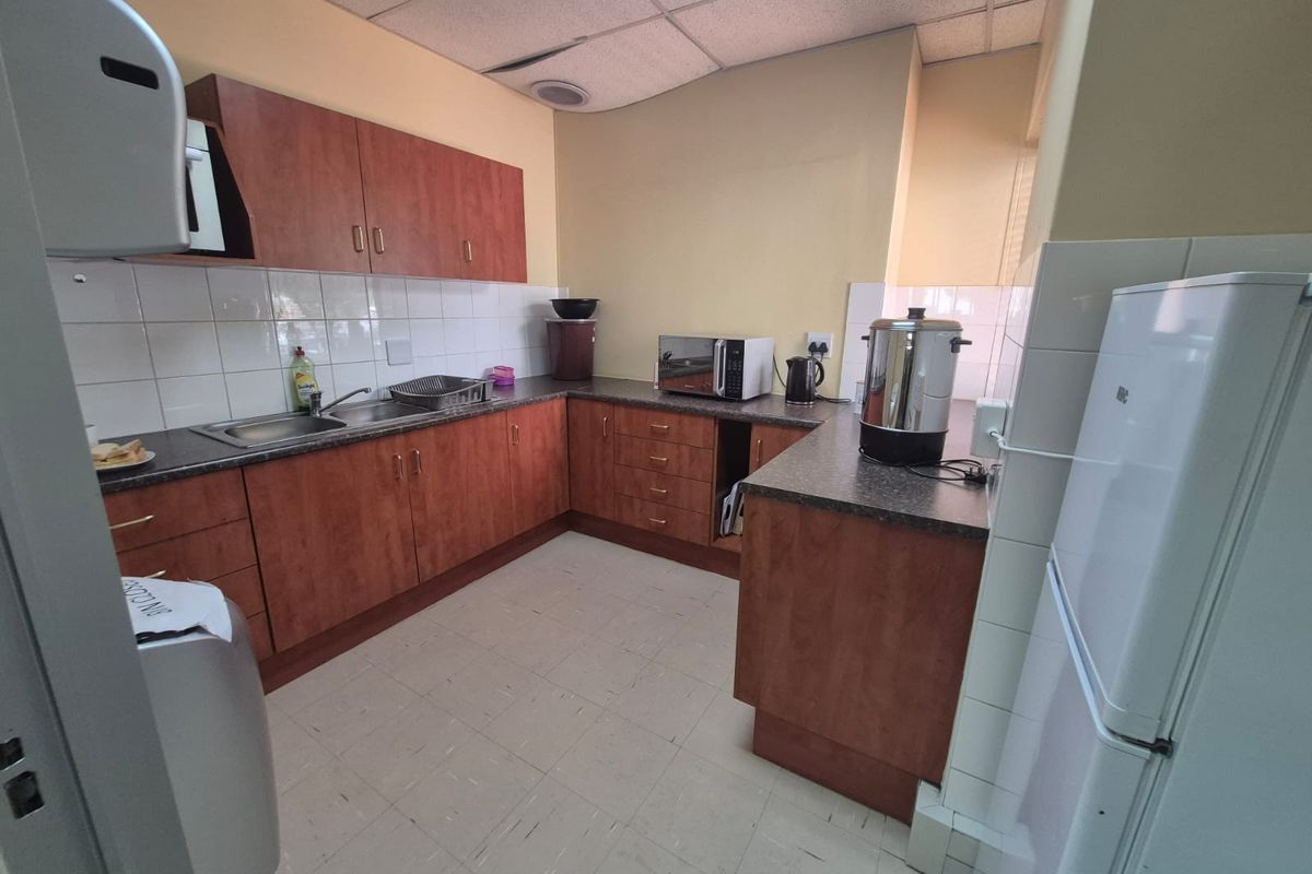 A functional office kitchenette featuring laminate cabinetry, tiled splashbacks, and a stainless steel sink, providing essential staff amenities.