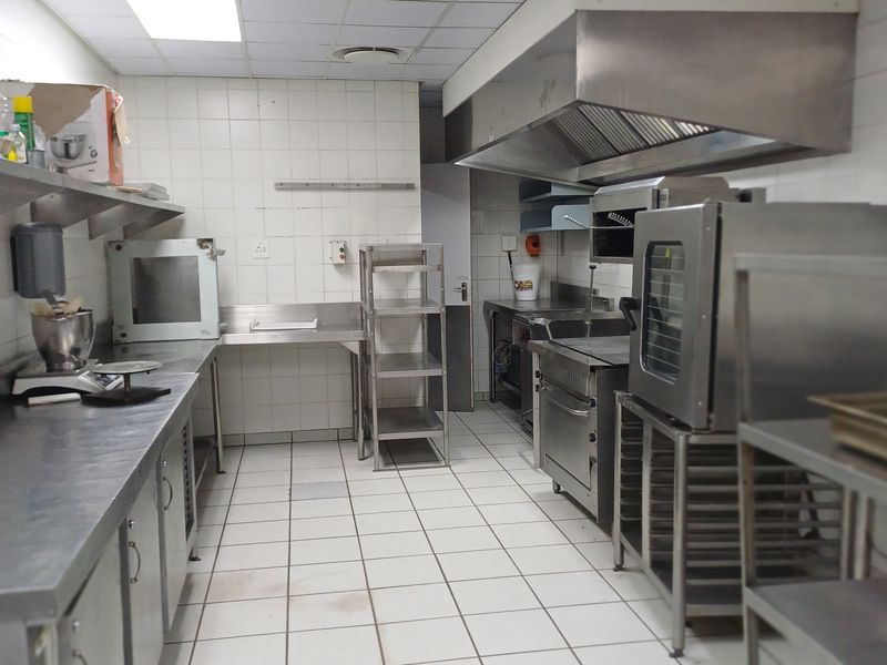 A functional commercial kitchen space featuring stainless steel work surfaces, industrial-grade extractor hood, tiled walls, and durable floor tiling.