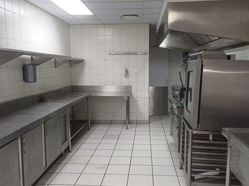 A functional commercial kitchen space featuring stainless steel work surfaces, integrated cabinetry, a professional extractor hood, and durable tiled finishes throughout.