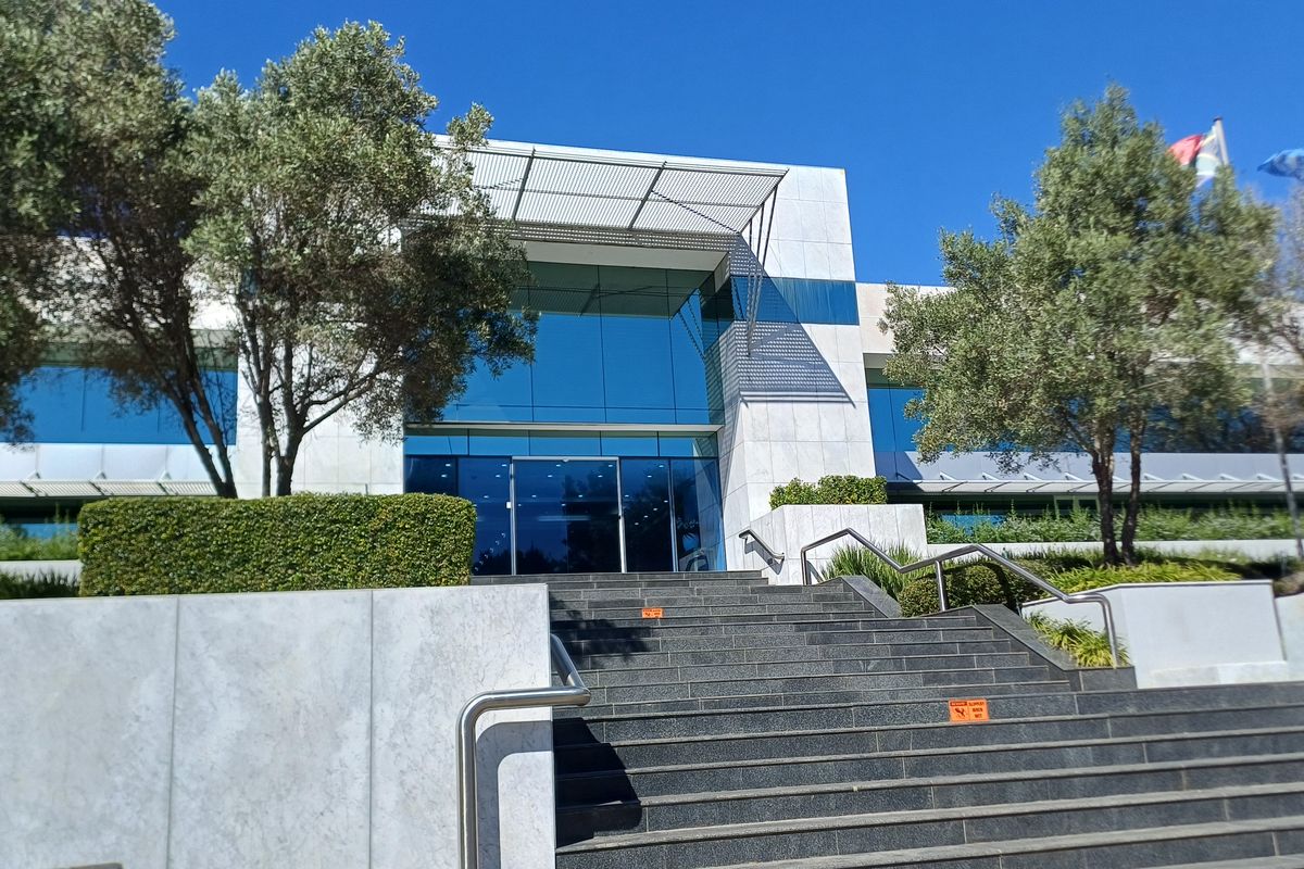 Modern office building entrance featuring a prominent stone-clad facade, glass curtain wall, metal canopy, and a wide stone staircase with stainless steel handrails.
