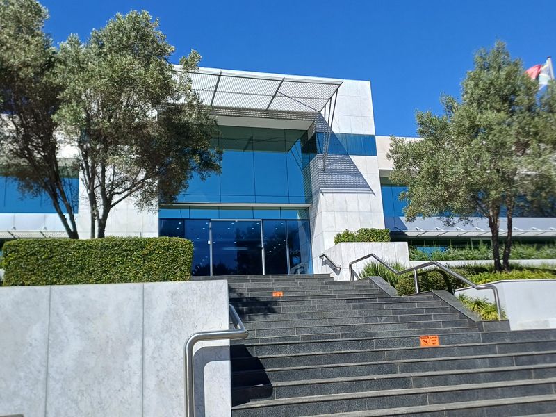Modern office building entrance featuring a prominent stone-clad facade, glass curtain wall, metal canopy, and a wide stone staircase with stainless steel handrails.