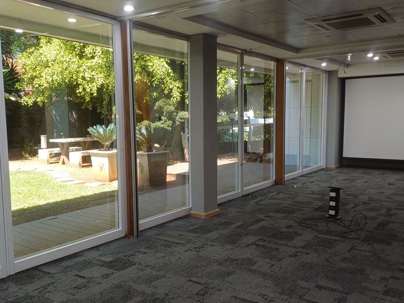 Spacious office area featuring large glass sliding doors with garden views, recessed lighting, ducted air conditioning, and a built-in projector screen.