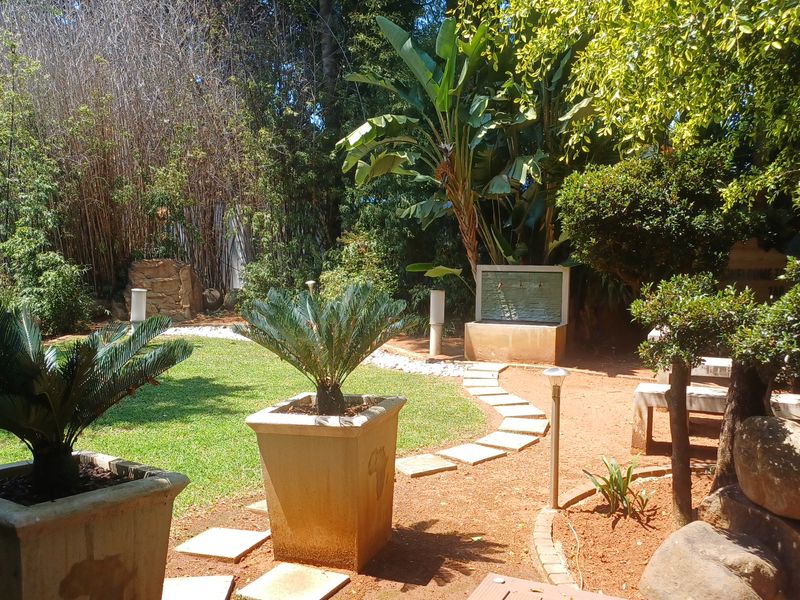 A well-maintained landscaped garden featuring a stone water feature, paved pathways, and established greenery, providing a tranquil outdoor space.