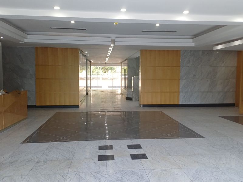 Spacious office building entrance lobby featuring polished marble flooring, wood paneling, and a built-in reception desk with recessed ceiling lighting.