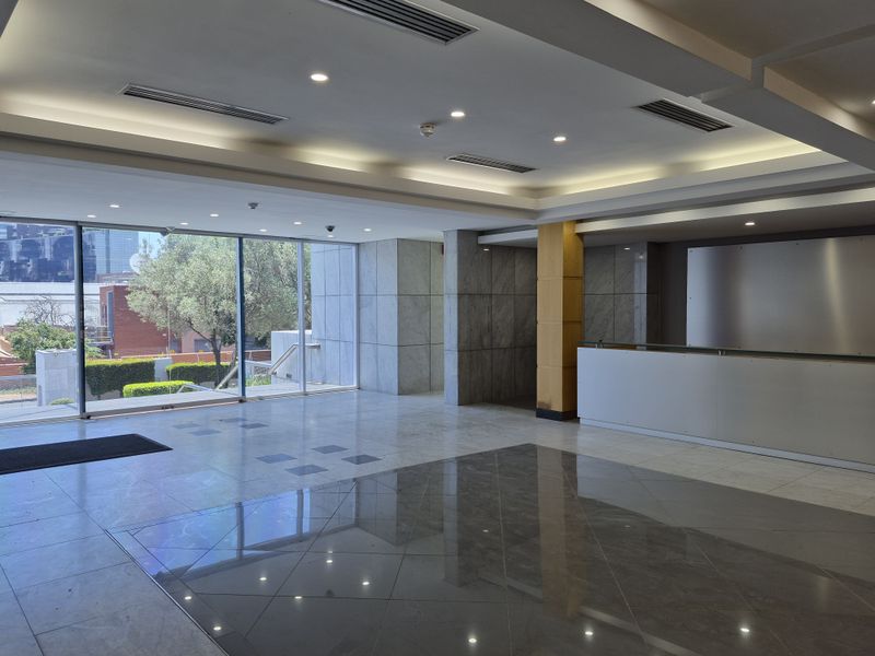 Spacious modern office building entrance lobby featuring polished marble flooring, integrated reception desk, and large floor-to-ceiling windows with natural light.