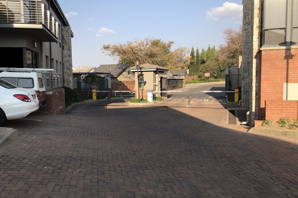 Entrance to the office complex featuring a secure boom gate, brick paved driveway, and modern building facade with stone cladding.