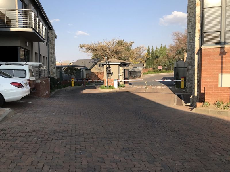 Entrance to the office complex featuring a secure boom gate, brick paved driveway, and modern building facade with stone cladding.