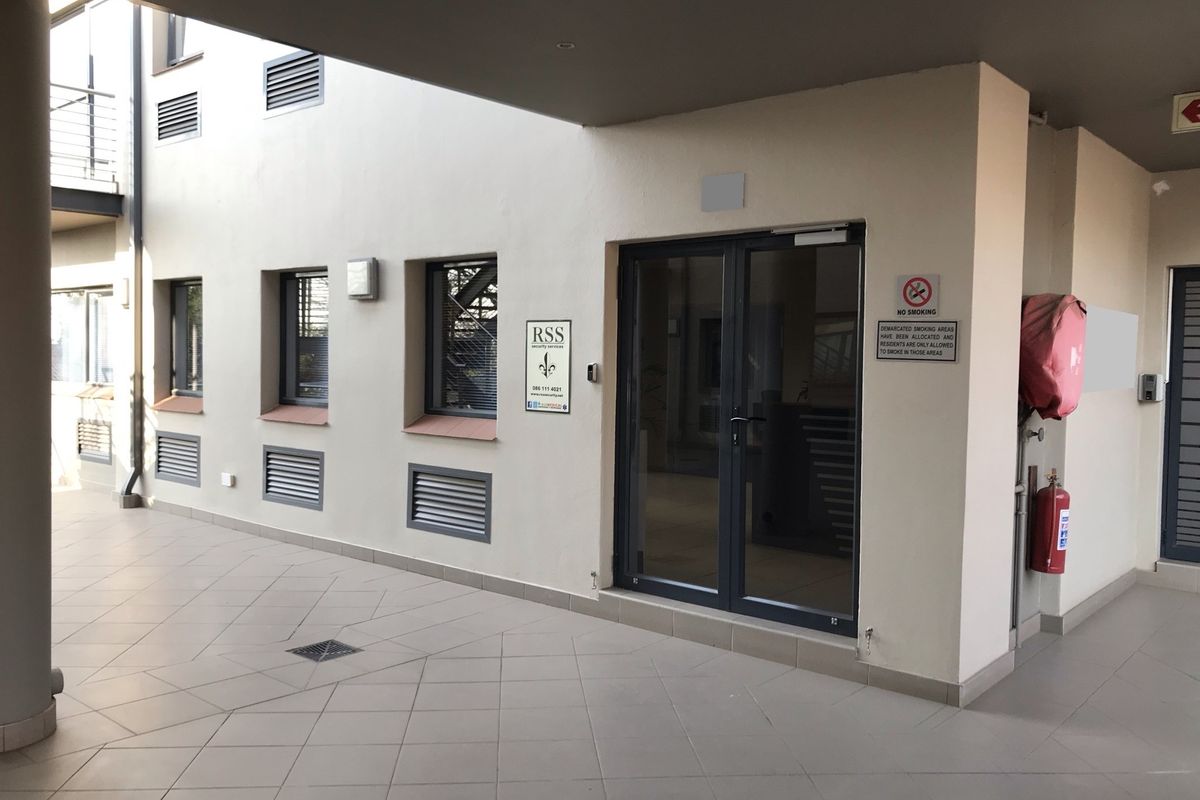 A clean, covered office building entrance featuring tiled flooring, double glass doors, and integrated fire safety equipment.