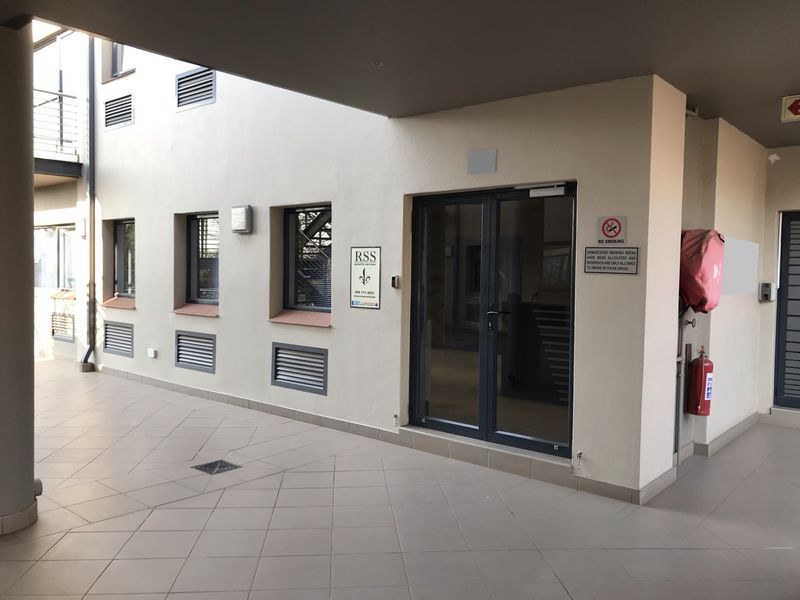 A clean, covered office building entrance featuring tiled flooring, double glass doors, and integrated fire safety equipment.