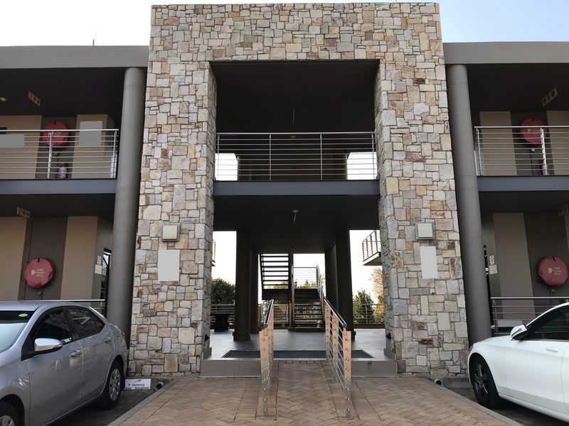 Modern office building exterior featuring a prominent stone-clad entrance, stainless steel balustrades, and paved access with integrated fire safety equipment.
