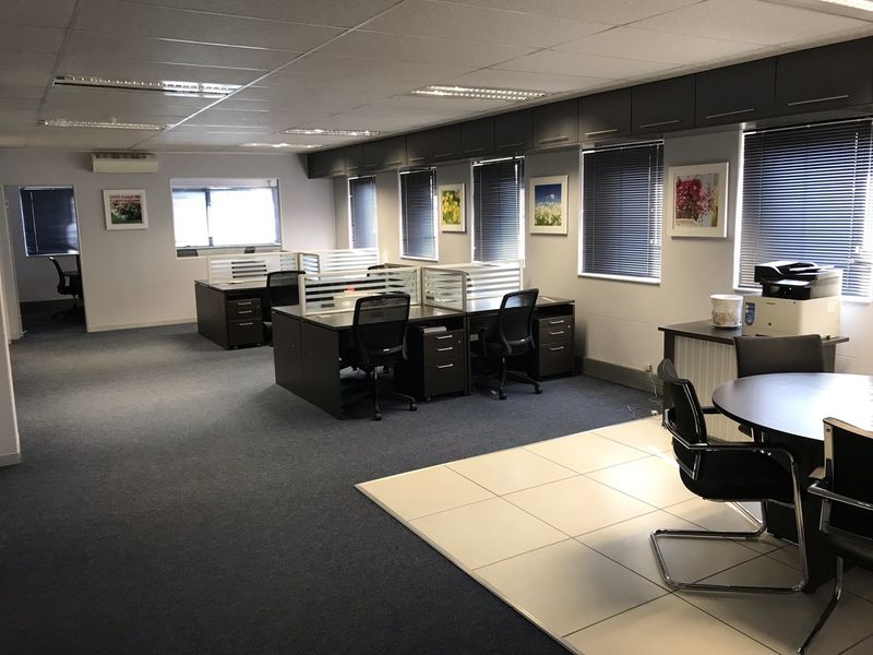 A spacious, well-maintained open-plan office featuring suspended ceilings, recessed lighting, built-in overhead storage, and a mix of carpet and tiled flooring.