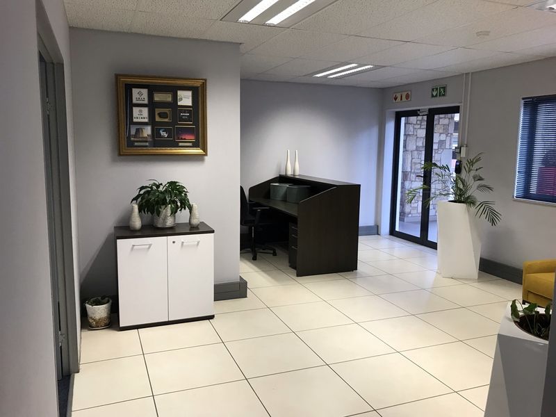 A professional office reception area featuring tiled flooring, a suspended ceiling with recessed lighting, and a glass entrance door.