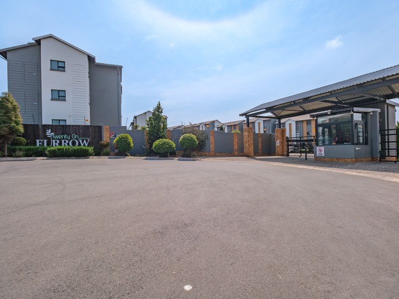 The entrance to the Twenty On Furrow complex, featuring a secure gated access point, guard house, and paved driveway.